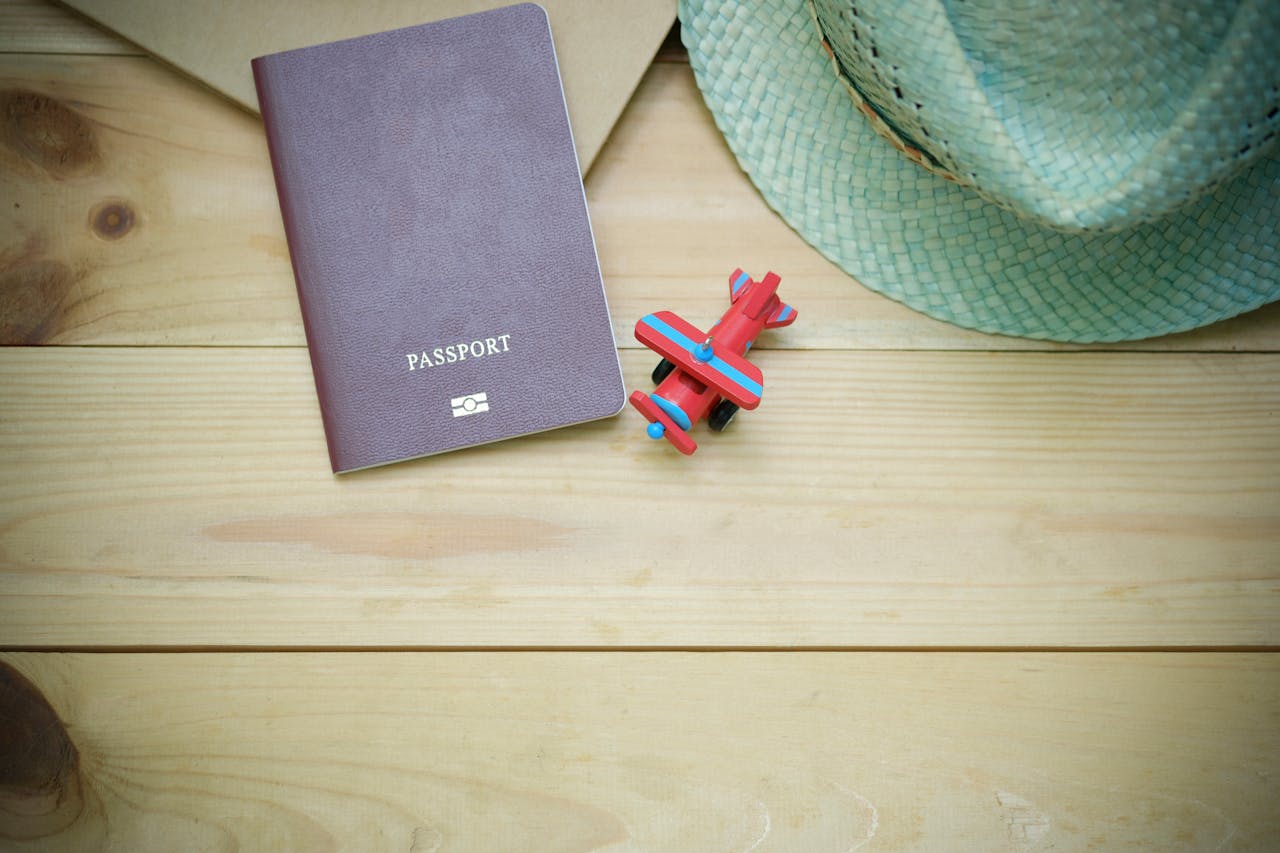 ours-journey Flat lay of a passport, straw hat, and toy airplane on a wooden surface.