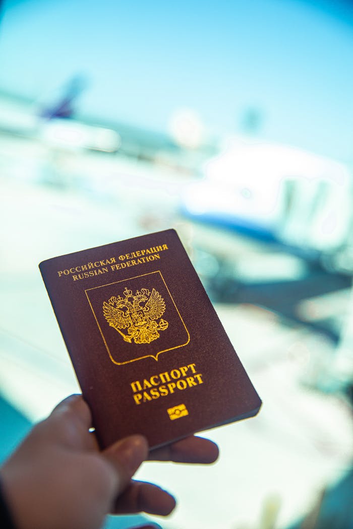 services-02 Close-up of a Russian passport being held near an airport gate window with blurred aircraft in the background.