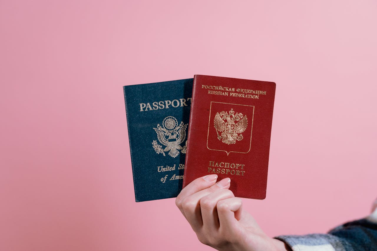 hero-img-02 Close-up of a hand holding American and Russian passports on a pink background.